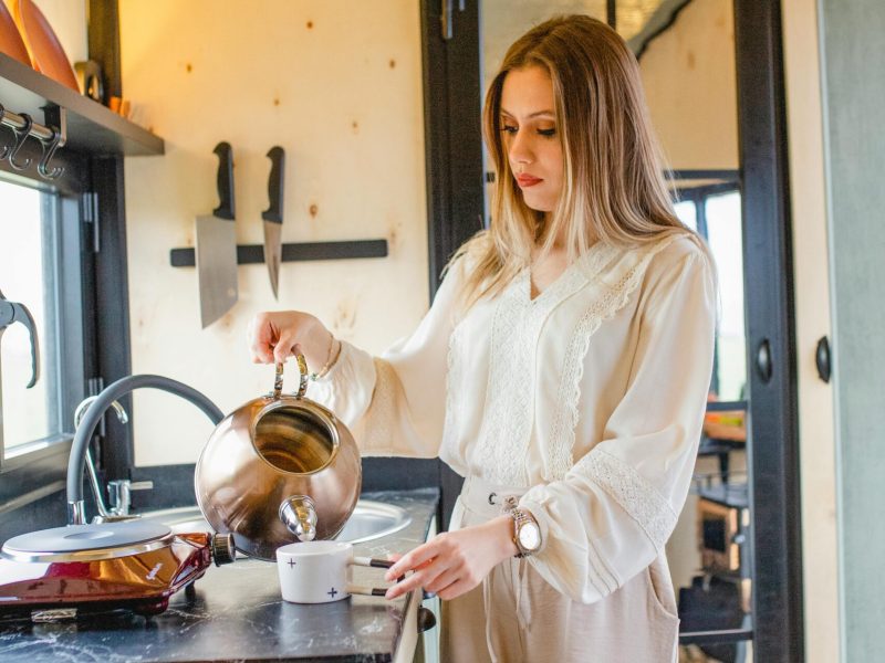 A woman pours tea from a kettle in a stylish tiny house kitchen, capturing a moment of modern living.